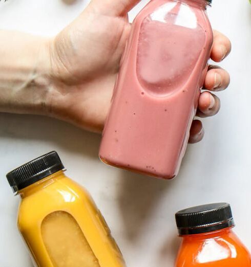 Detox Drinks - Person Holding Bottle of Smoothie Beside Green Leaves, Carrots and Berries