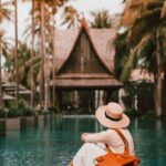 Destinations - Anonymous female relaxing near calm rippling water of pond surrounded with houses and palm trees