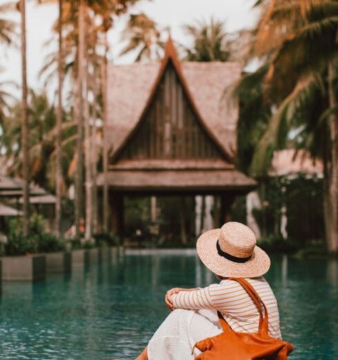 Destinations - Anonymous female relaxing near calm rippling water of pond surrounded with houses and palm trees