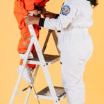 Activities - Content ethnic children in spacesuits standing on stepladder