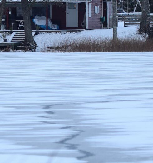 Retreats - Winter Landscape with a House by a Forest and Dry Grass by a Frozen Lake