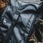 Waterproof Backpack - From above of stylish black rucksack with image on dry terrain among growing plants in forest