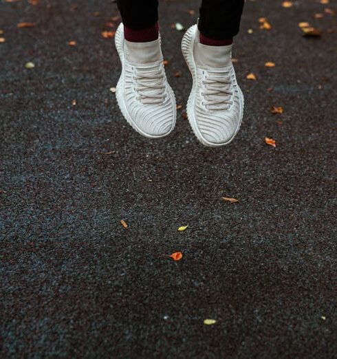 Compression Socks - Feet of faceless person in white sneakers jumping above dark surface of sports ground