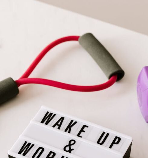 Fitness Accessories - From above composition of dumbbells and massage double ball and tape and tubular expanders surrounding light box with wake up and workout words placed on white surface of table