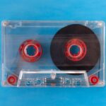 Guides - One transparent compact audio cassette with visible tape and red inner reels isolated on blue background. Top down view flat lay with empty space for text