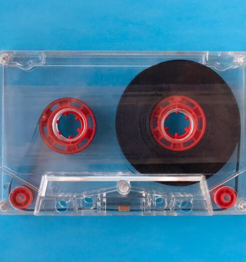 Guides - One transparent compact audio cassette with visible tape and red inner reels isolated on blue background. Top down view flat lay with empty space for text