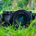 Photography - Black Sony Dslr Camera on Green Grass in Front of Brown and Green Mountain