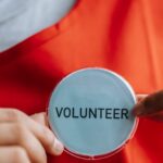 Volunteer - Smiling ethnic woman showing volunteer sign on red apron