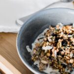 Muesli - From above of bowl with muesli with milk and small teapot placed on wooden tray placed on bed in morning time