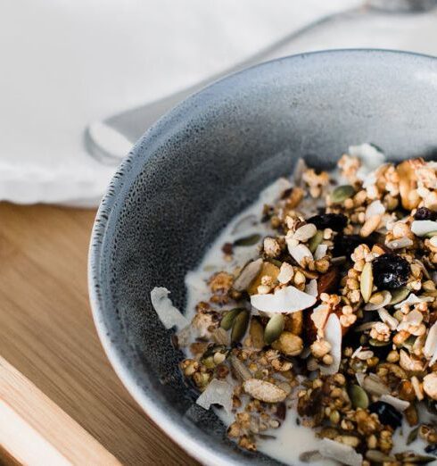 Muesli - From above of bowl with muesli with milk and small teapot placed on wooden tray placed on bed in morning time