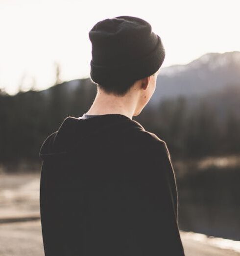 Beanie - Selective Focus Photography of Man Standing on Brown Soil Facing Body of Water