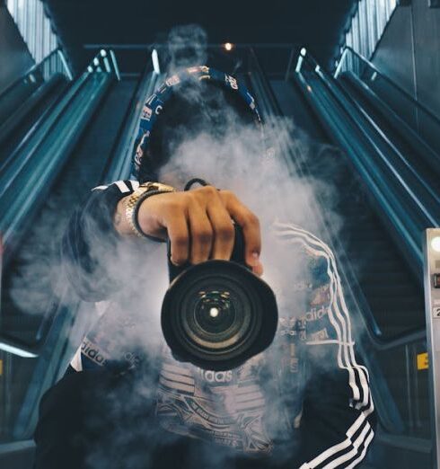 Wear - Man Holding Camera While Squating With Smoke on Face Inside Building