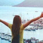 Traveling - Woman Raising Her Hands Facing Cityscape Near Body of Water