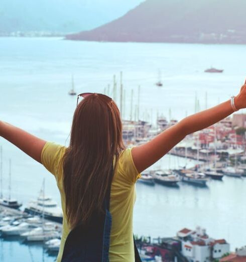 Traveling - Woman Raising Her Hands Facing Cityscape Near Body of Water