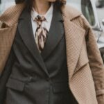 Outerwear - A woman in a suit and hat walking down the street with a suitcase