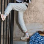 Outfits - Woman in Blue Shirt and White Pants Leaning on Black Metal Gate