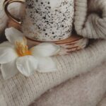 Cardigans - Cup of Coffee Standing on Pile of Cardigans Decorated with Flowers