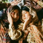 Scarves - Two Women Wearing Earth-toned Printed Tops And Scarves Lying On A Pile Of Clothes