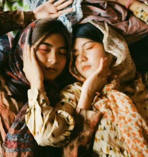 Scarves - Two Women Wearing Earth-toned Printed Tops And Scarves Lying On A Pile Of Clothes