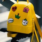 Bags - Yellow Backpack With Five Assorted Stickers on Grey Metal Stairway Rail