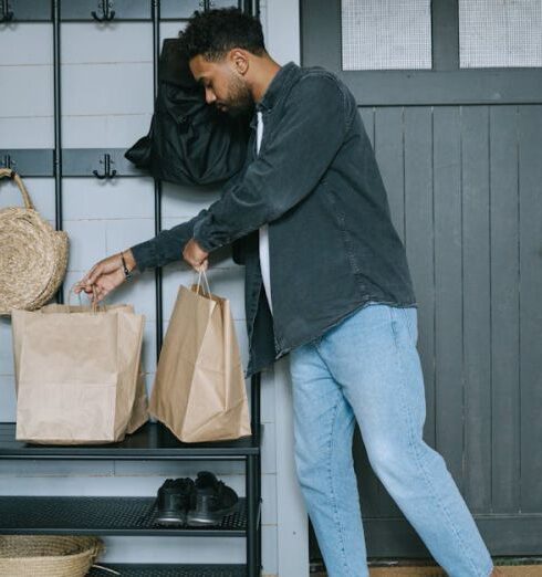 Clogs - Man in Black Long Sleeve Shirt and Blue Denim Jeans Standing Beside Black Wooden Door