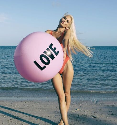 Swimsuit - Woman Wearing Orange Swimsuit While Holding Pink Inflatable Beside Body of Water