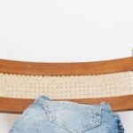 Jeans - Stack of blue jeans of different shades on modern wooden chair against white wall