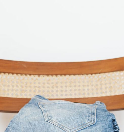 Jeans - Stack of blue jeans of different shades on modern wooden chair against white wall