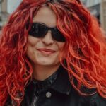 Jackets - A woman with red hair and sunglasses standing in a city