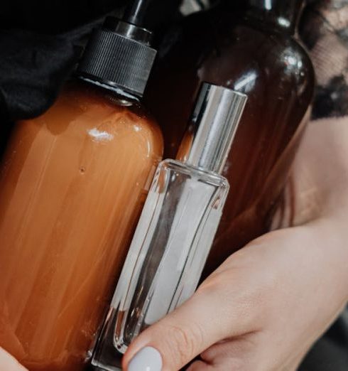 Skincare - Person in Black Silk Robe Holding Glass Pump Bottles