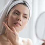 Skincare - Selective Focus Portrait Photo of Woman With a Towel on Head Looking in the Mirror