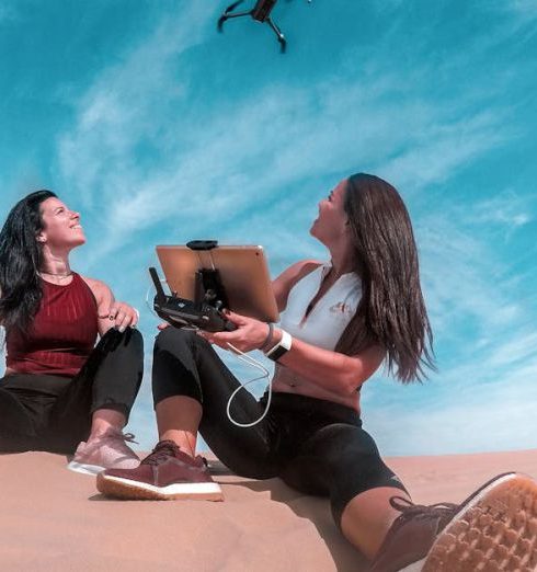 Gadgets - Two Woman Sitting On Sand While Playing Drone