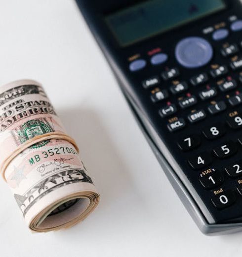 Electronics Bundles - From above of modern electronic calculator with small display and buttons of different colors near roll of dollar bills on marble surface