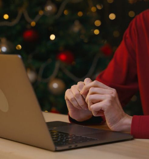 Tech Gifts - Woman Sitting at a Table and Using a Laptop on the Background of a Christmas Tree