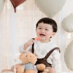 Baby Shower Gifts - Laughing Boy Sitting with a Teddy Bear at his Birthday Party