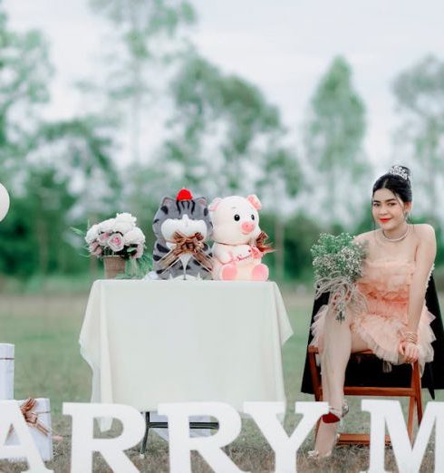 Meaningful Gifts - Young Woman in a Pink Dress Sitting at a Table with Stuffed Animals and Marry Me Sign