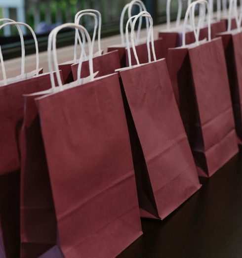 Corporate Gifts - Close-Up Shot of Maroon Paper Bags on a Table