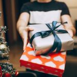 Home Gifts - Man Standing with Christmas Gifts next to Christmas Tree