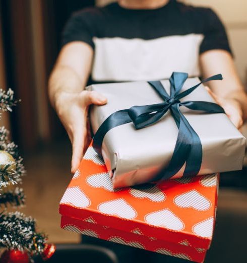 Home Gifts - Man Standing with Christmas Gifts next to Christmas Tree