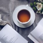 Poetry - White Ceramic Teacup With Saucer Near Two Books Above Gray Floral Textile