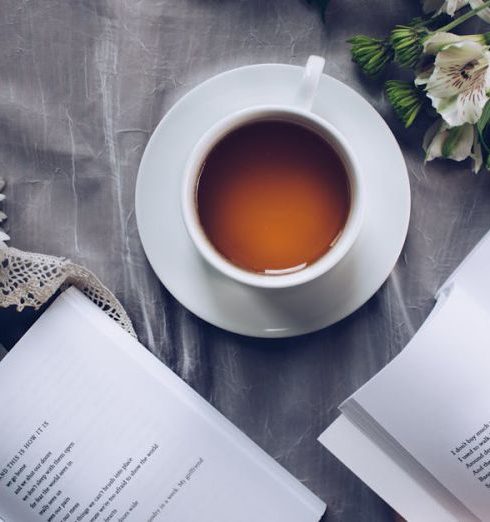 Poetry - White Ceramic Teacup With Saucer Near Two Books Above Gray Floral Textile