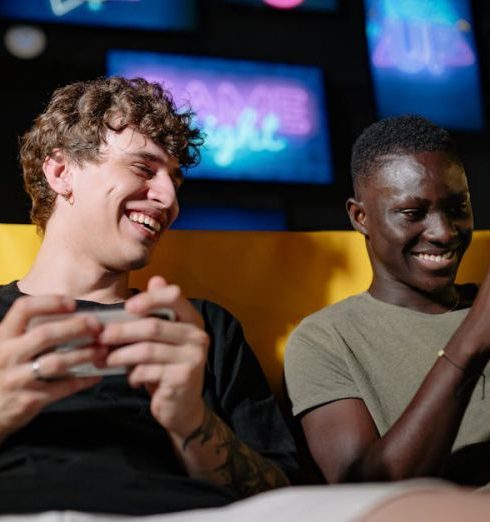 Gaming Gadgets - A Low Angle Shot of Men Sitting on the Couch while Holding their Mobile Phones