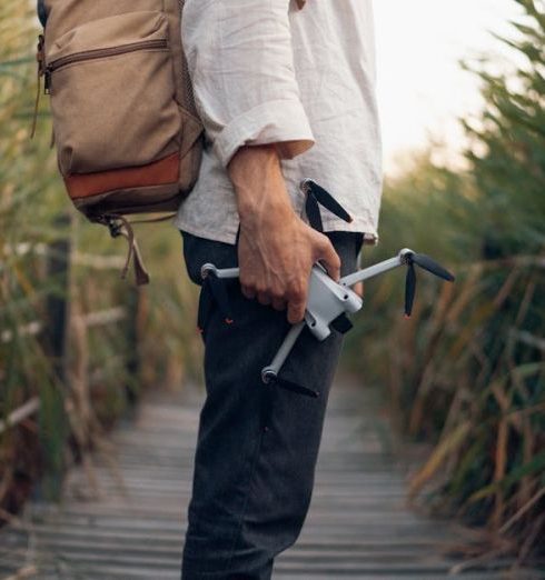 Outdoor Gadgets - A Man with a Backpack Holding a Drone