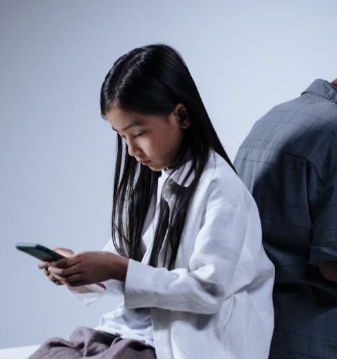 Kids Gadgets - Boy and Girl Sitting Back to Back Holding Smartphone