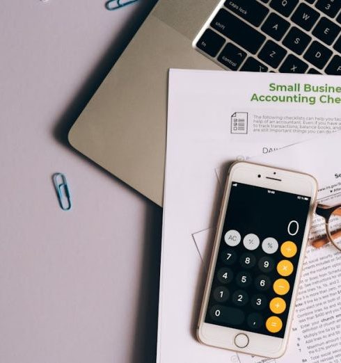 Budget Gadgets - A Mobile Phone and Eyeglasses on Top of the Documents Near the Laptop