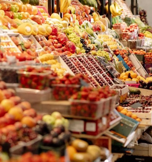 Grocery Stores - Woman in Red Clothes and Beret Walking Beside the Fruits Store