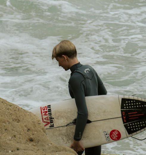 Surfing Gear - View of a Surfer Holding a Surfboard Walking on the Shore