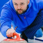 Winter Sports Gear - Pensive man sliding and holding stone with red handle on ice rink