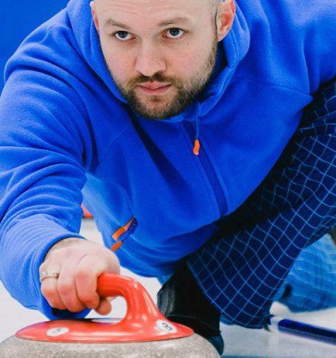 Winter Sports Gear - Pensive man sliding and holding stone with red handle on ice rink