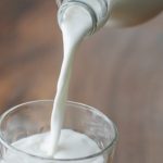 Organic Milk - Crop anonymous person with bottle pouring milk into ornamental transparent glass on wooden table at home